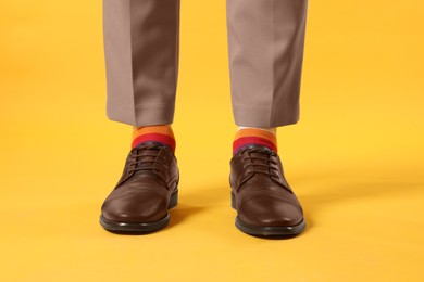 Photo of Man in stylish colorful socks, shoes and pants on yellow background, closeup