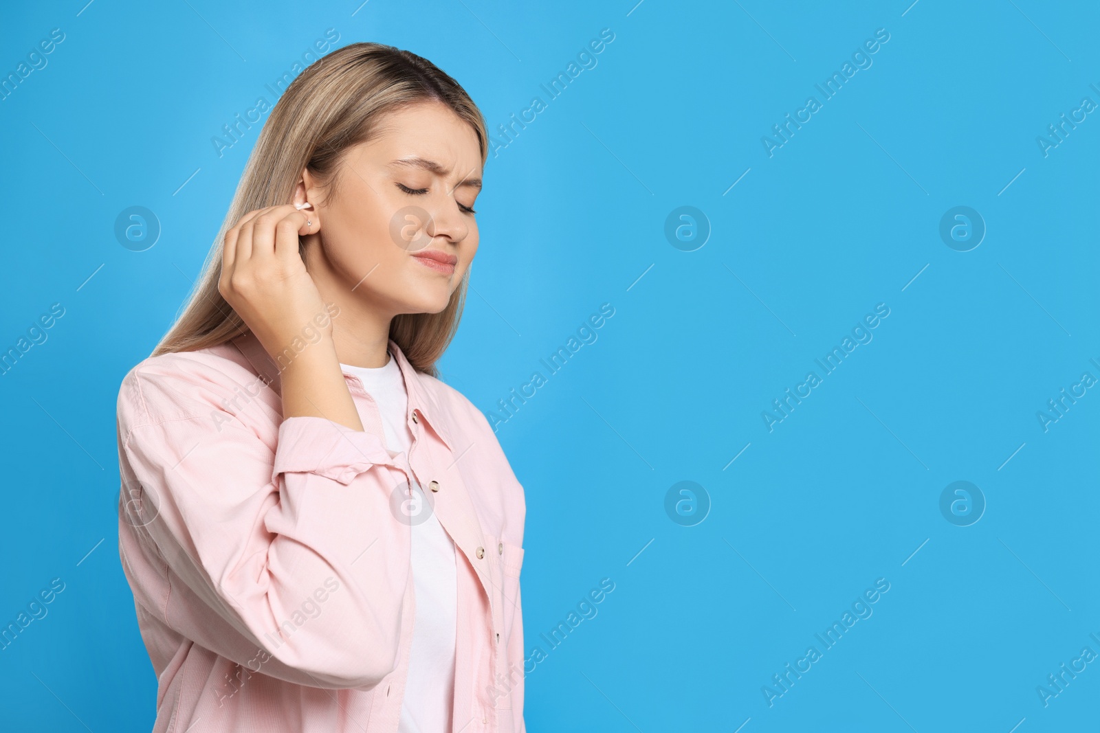 Photo of Young woman cleaning ear with cotton swab on light blue background. Space for text