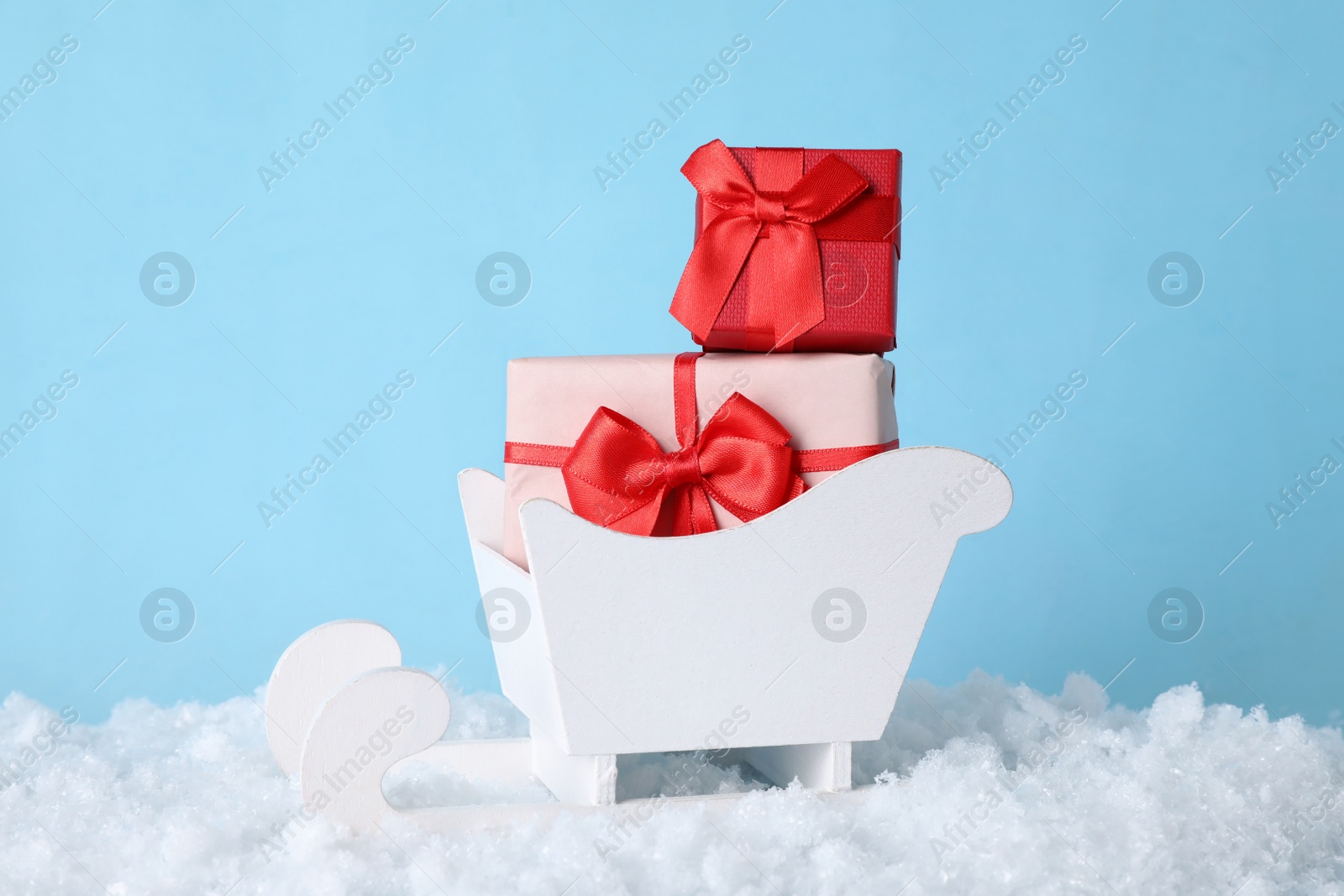 Photo of White wooden sleigh with Christmas gift boxes and artificial snow on light blue background