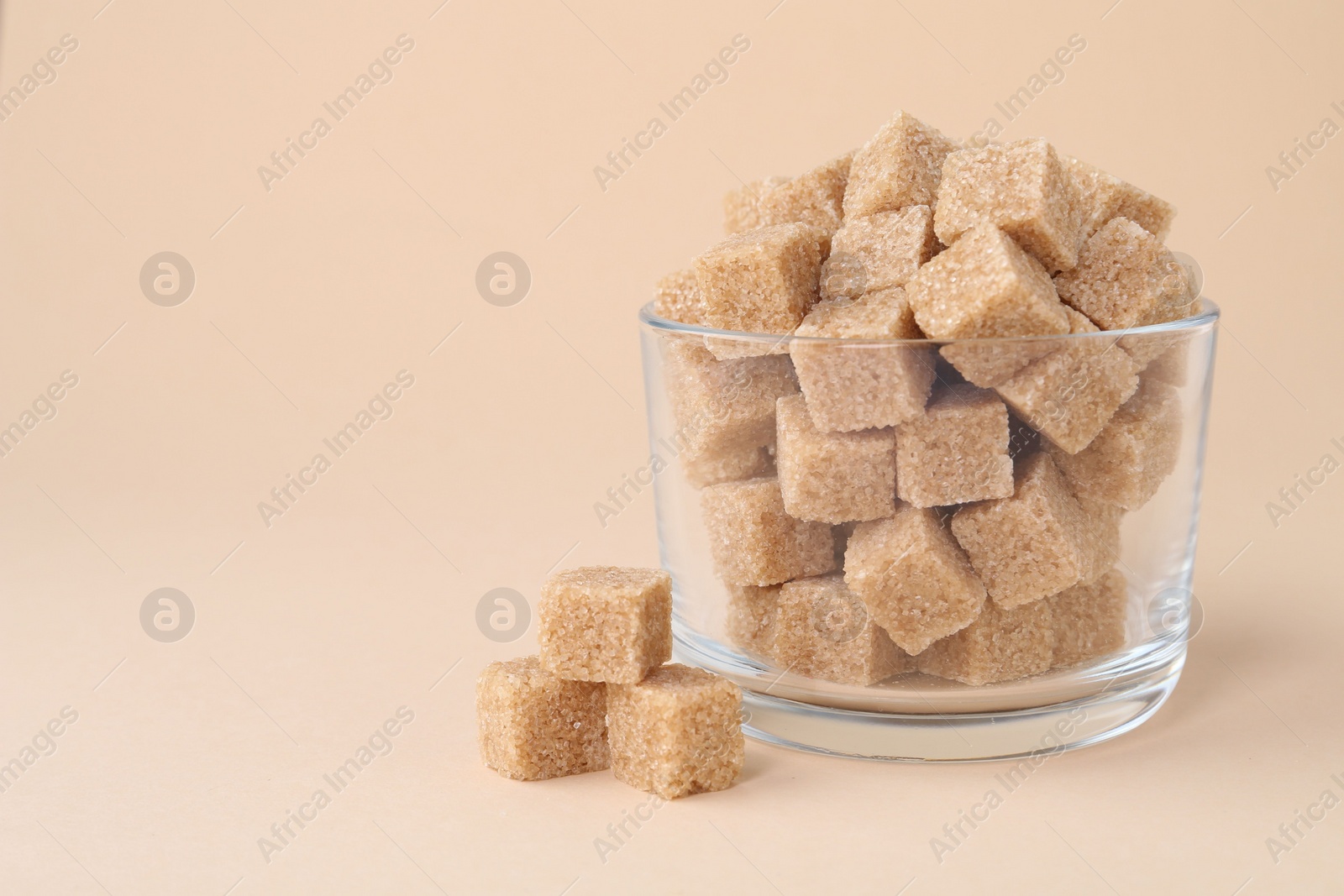 Photo of Brown sugar cubes in glass on beige background, closeup. Space for text