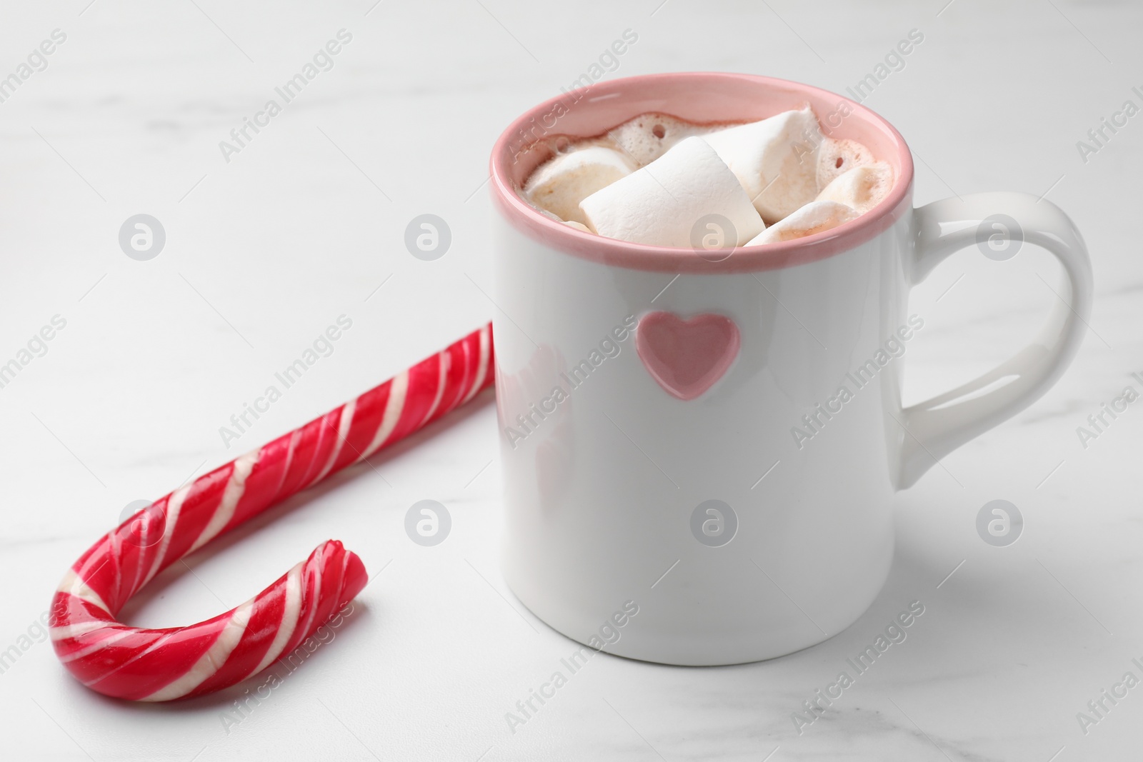 Photo of Tasty hot chocolate with marshmallows and candy cane on white marble table, closeup