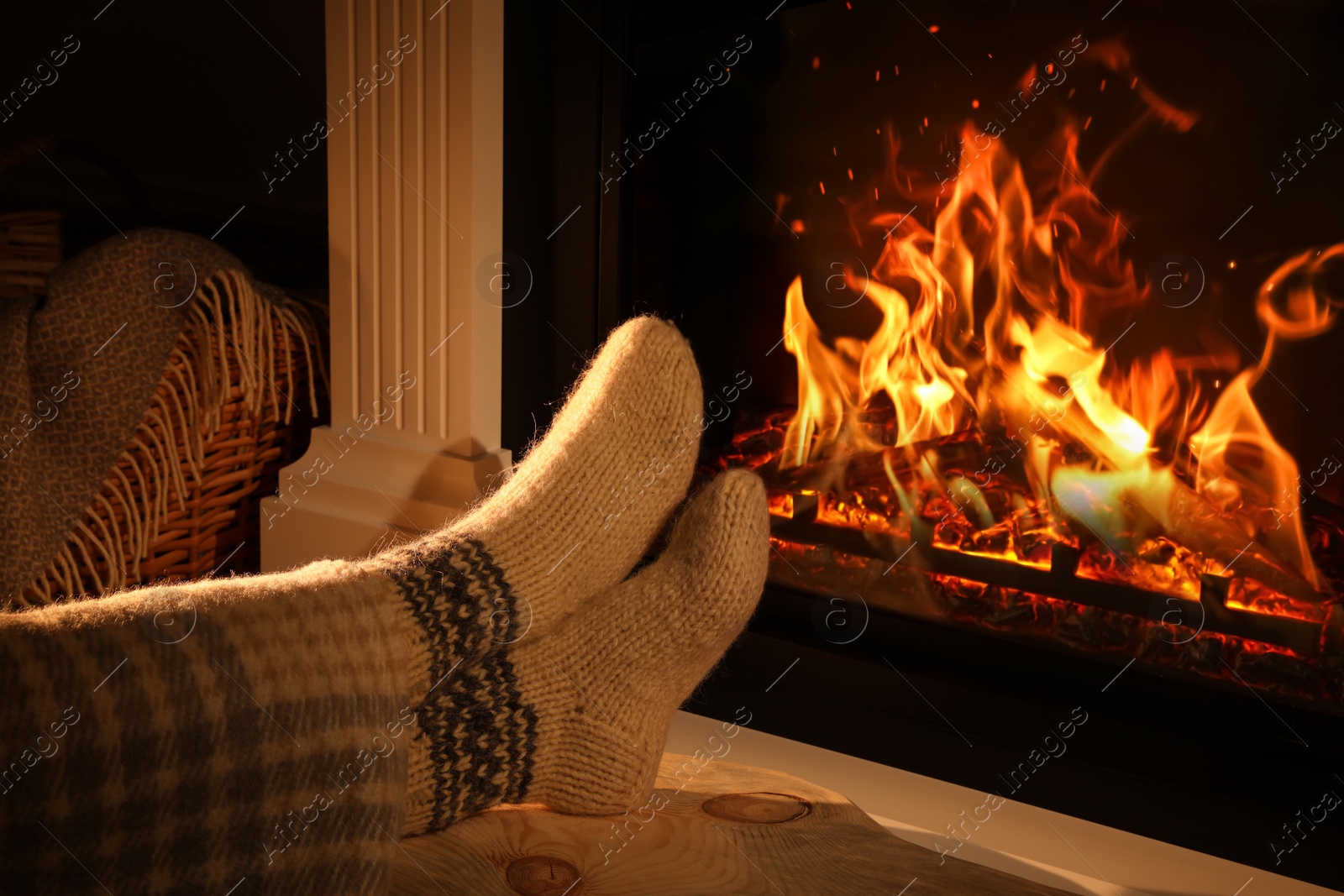 Photo of Woman in knitted socks near fireplace at home, closeup
