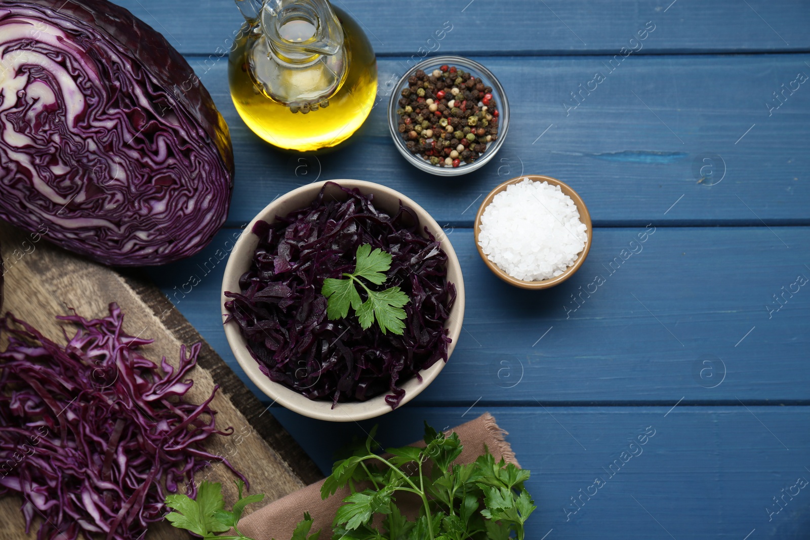 Photo of Tasty red cabbage sauerkraut with parsley and different ingredients on light blue wooden table, flat lay. Space for text