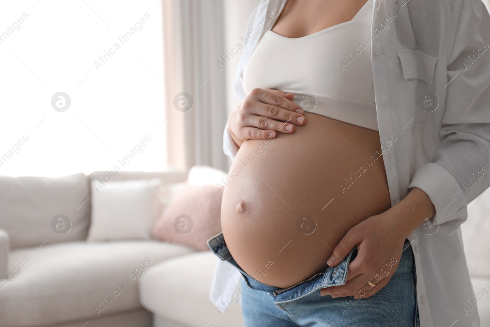 Photo of Pregnant young woman touching belly at home, closeup. Space for text