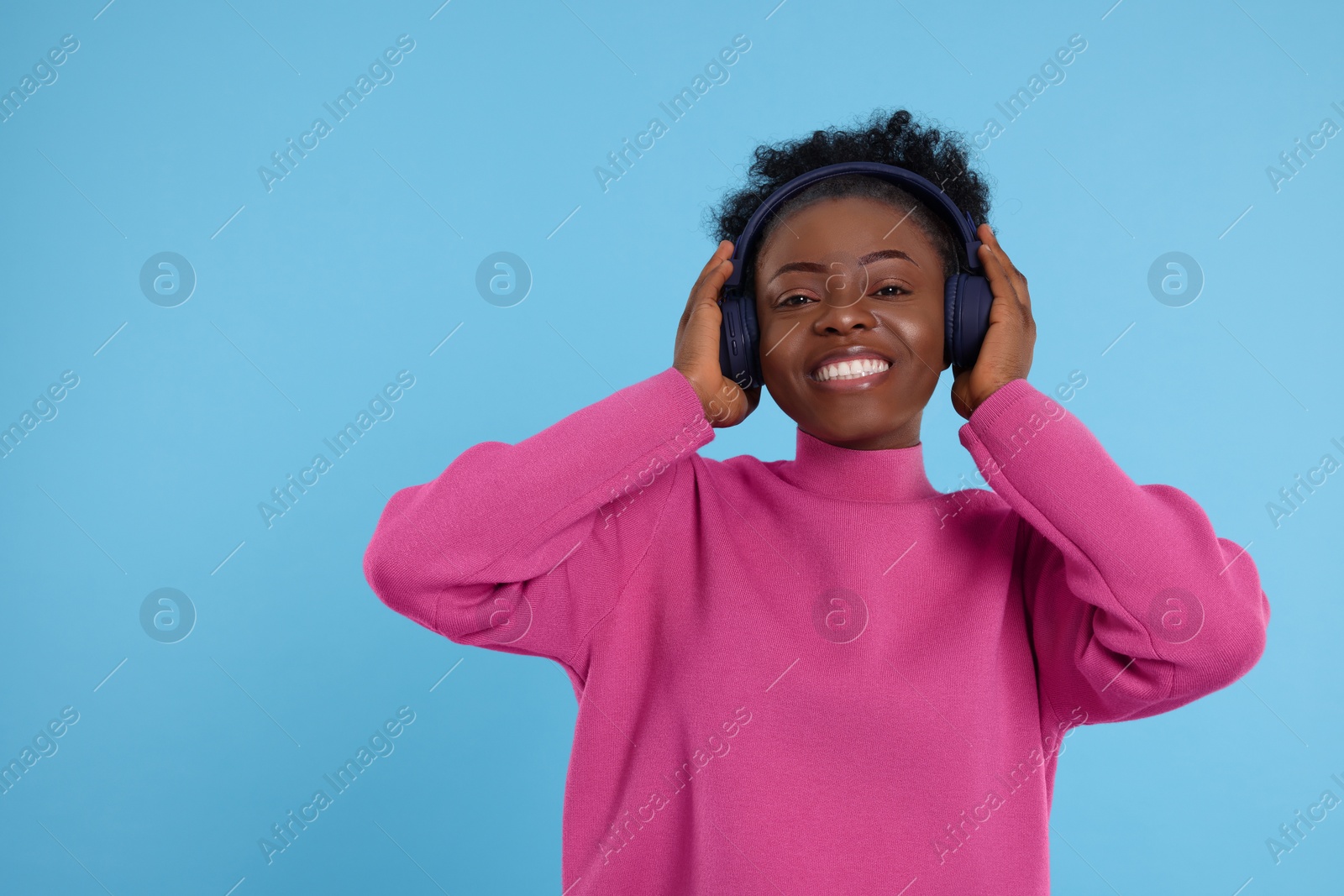 Photo of Young woman in headphones enjoying music on light blue background