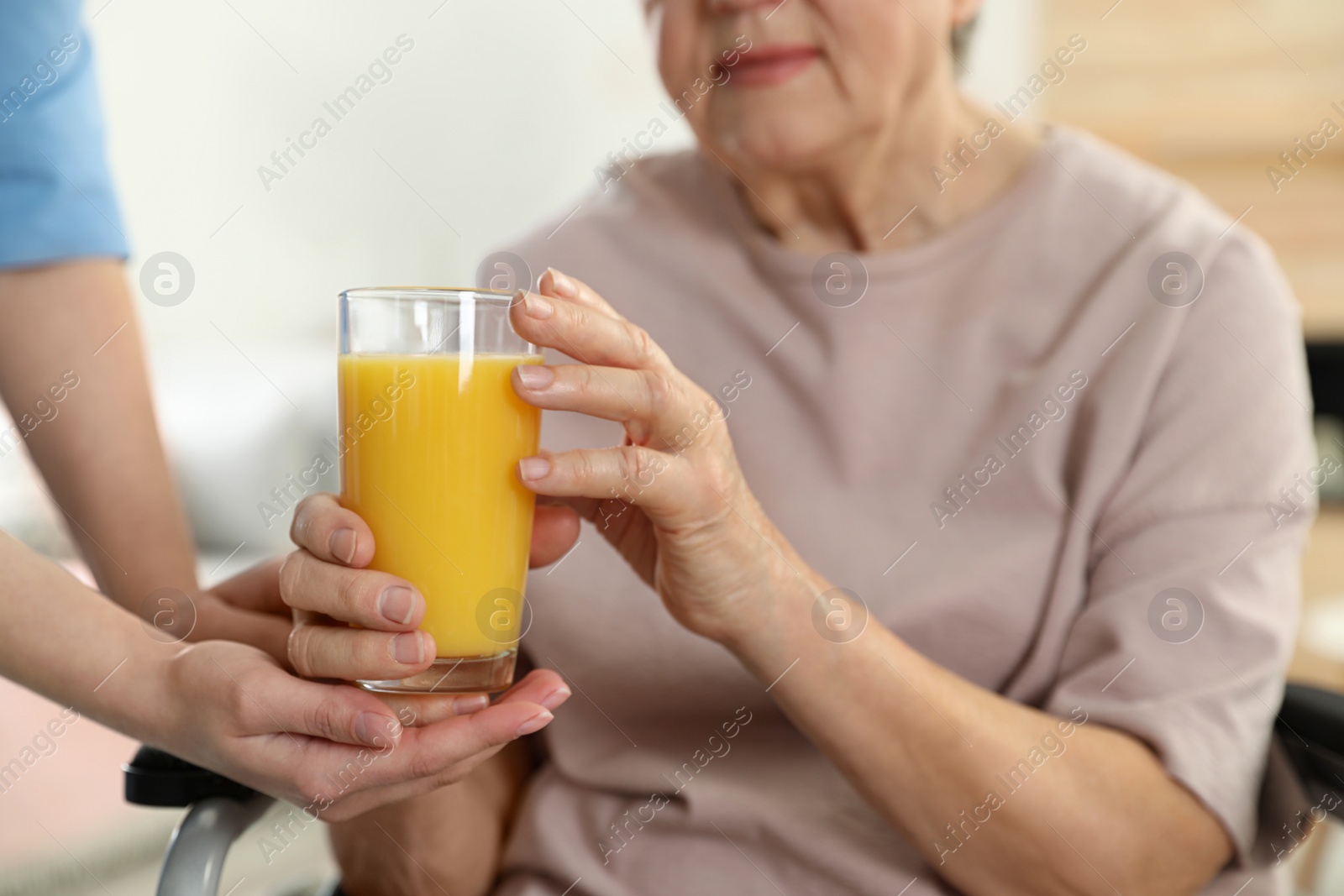 Photo of Nurse giving glass of juice to elderly woman indoors, closeup. Assisting senior people