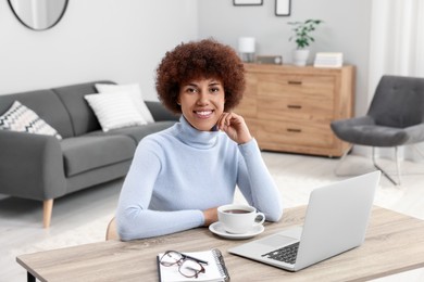 Photo of Beautiful young woman using laptop at wooden desk in room