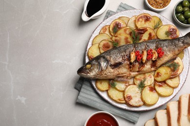 Photo of Plate with delicious roasted sea bass fish and potatoes on light grey table, flat lay. Space for text