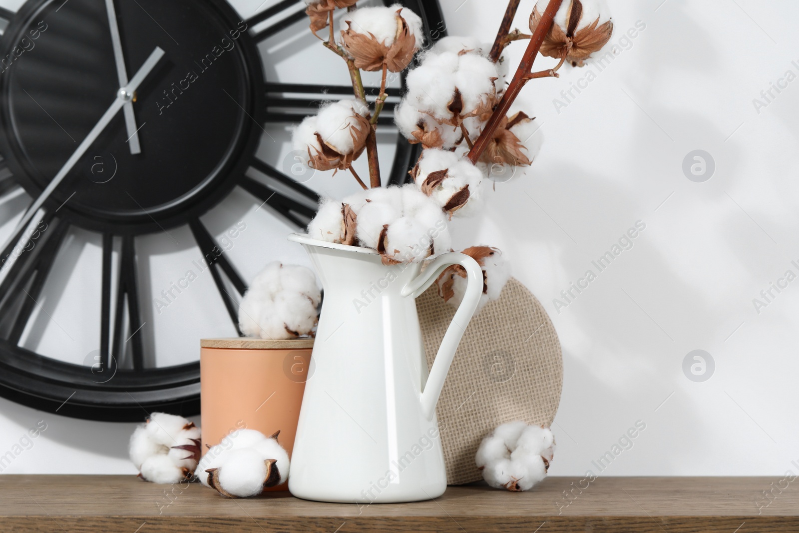 Photo of Cotton branches with fluffy flowers and home decor on wooden table near white wall