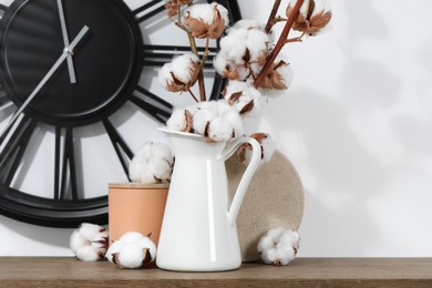 Photo of Cotton branches with fluffy flowers and home decor on wooden table near white wall