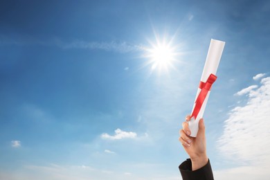 Image of Graduated student holding diploma against blue sky on sunny day, closeup