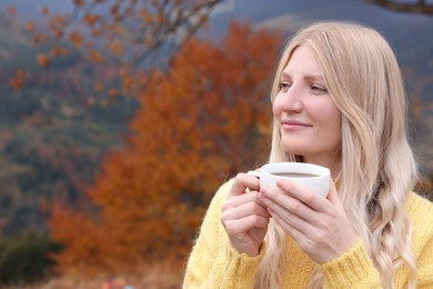 Photo of Young woman with cup of hot drink outdoors in autumn. Space for text