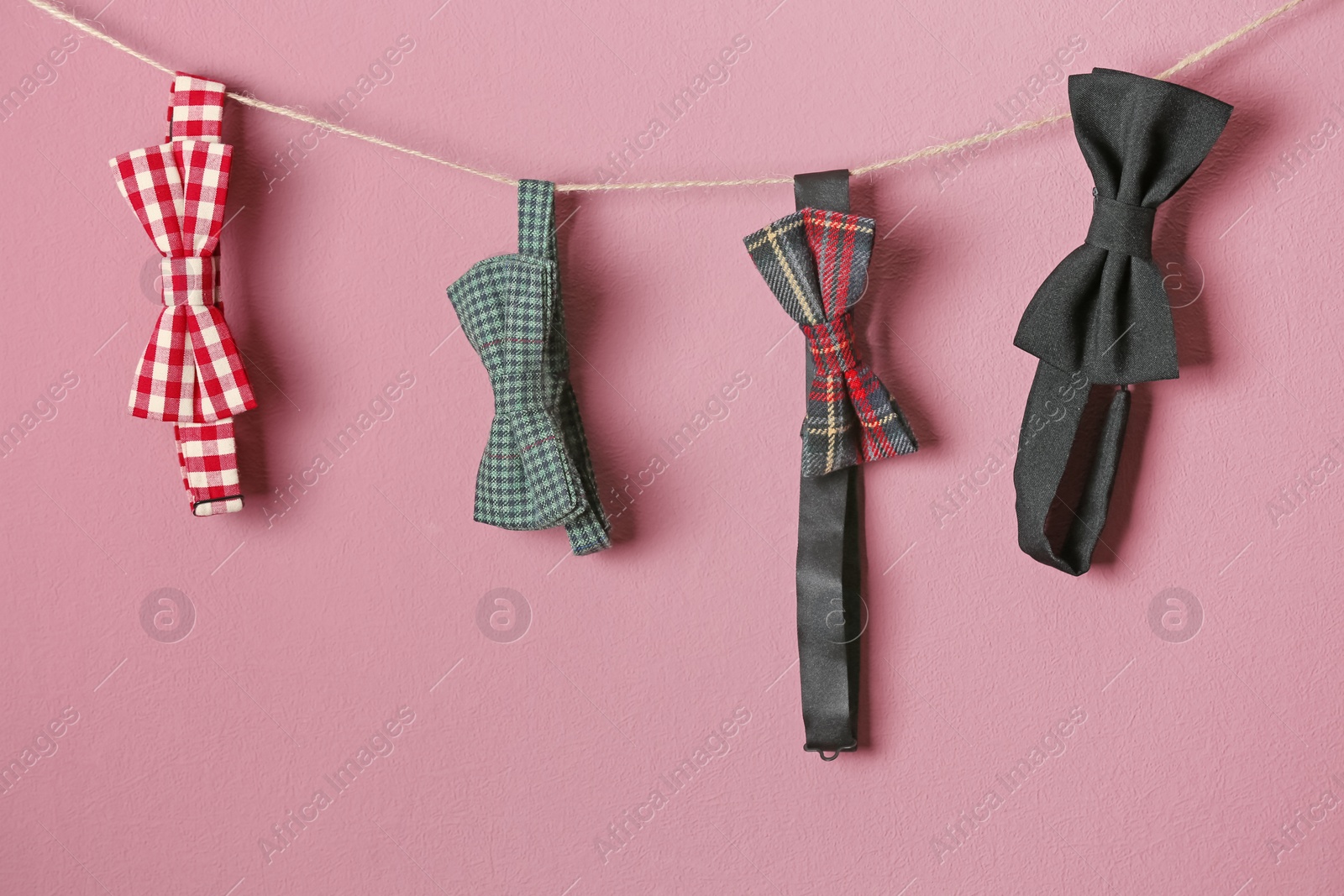 Photo of Bow ties hanging on rope against color background