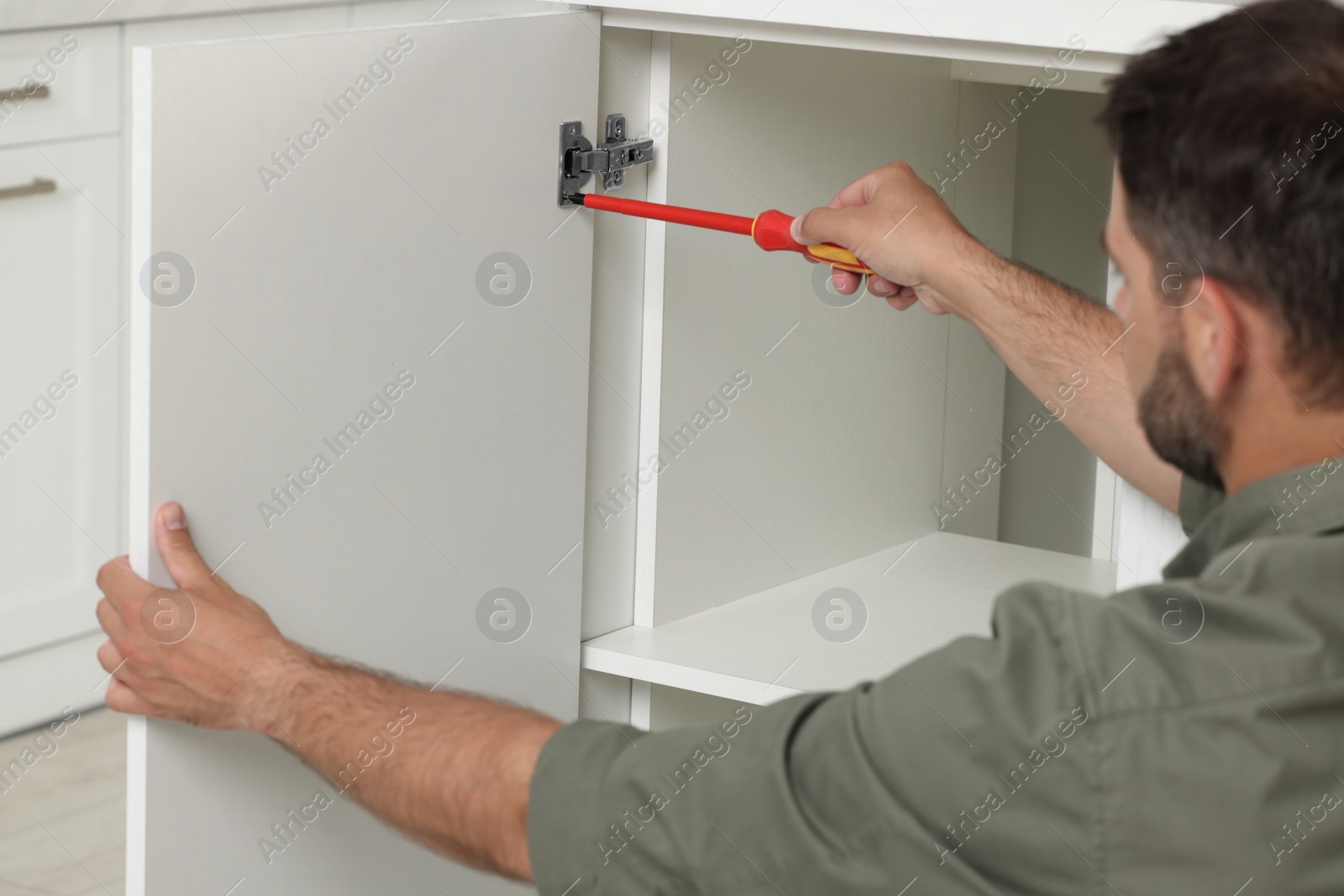 Photo of Man with electric screwdriver assembling furniture indoors, closeup