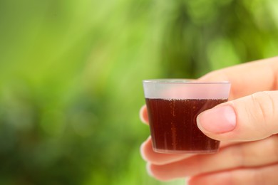 Woman holding measuring cup with syrup on blurred background, closeup and space for text. Cold medicine