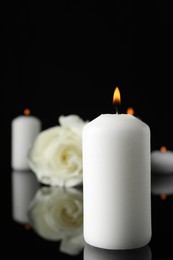 Photo of Burning candle on black mirror surface in darkness, closeup with space for text. Funeral symbol