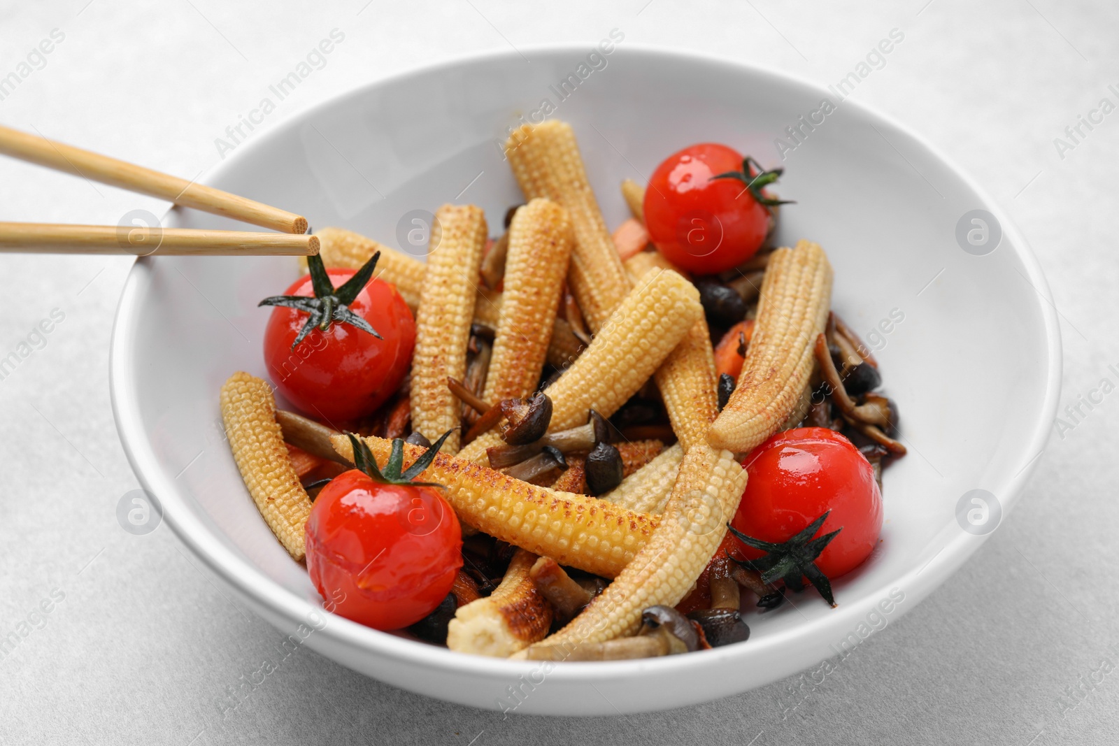 Photo of Tasty roasted baby corn with tomatoes and mushrooms on light grey table, closeup