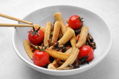 Tasty roasted baby corn with tomatoes and mushrooms on light grey table, closeup