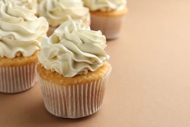 Photo of Tasty vanilla cupcakes with cream on beige table, closeup. Space for text