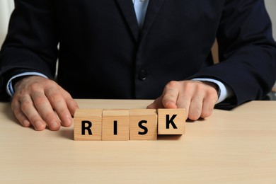 Photo of Businessman making word Risk of cubes at wooden table, closeup