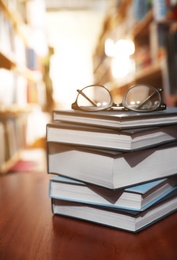 Photo of Stack of books and glasses on table in library