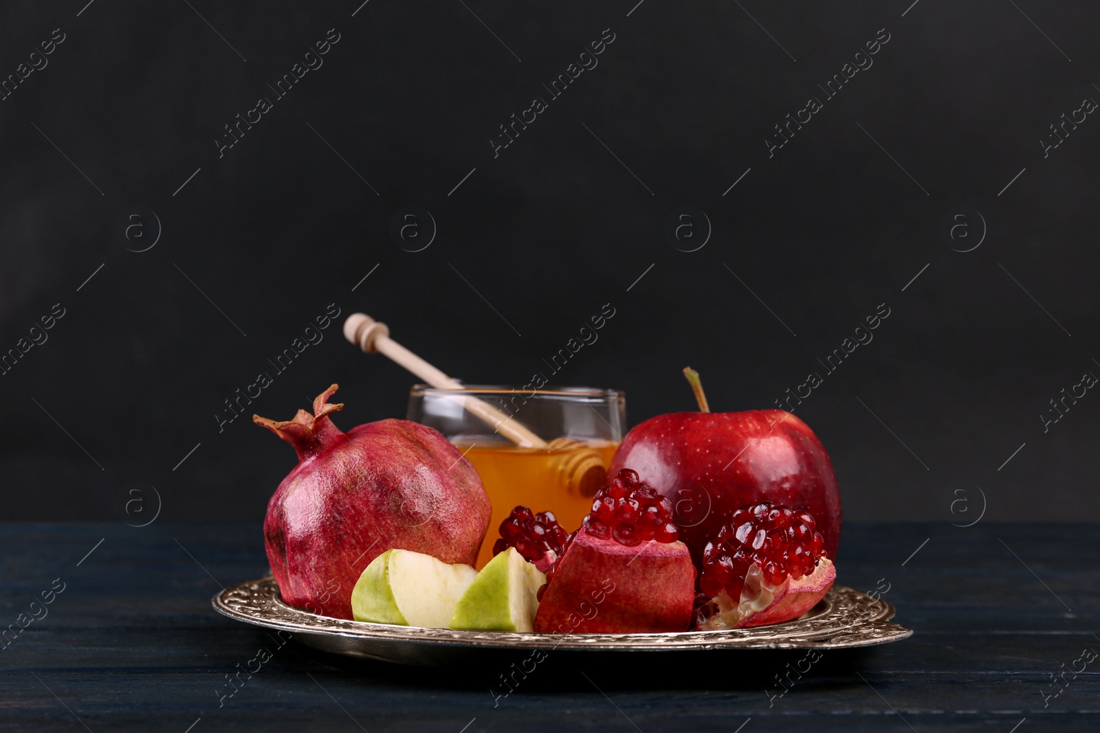 Photo of Honey, apples and pomegranate on dark blue wooden table. Rosh Hashanah holiday