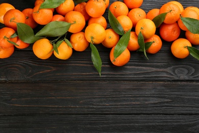Fresh ripe tangerines with green leaves on black wooden table, flat lay. Space for text