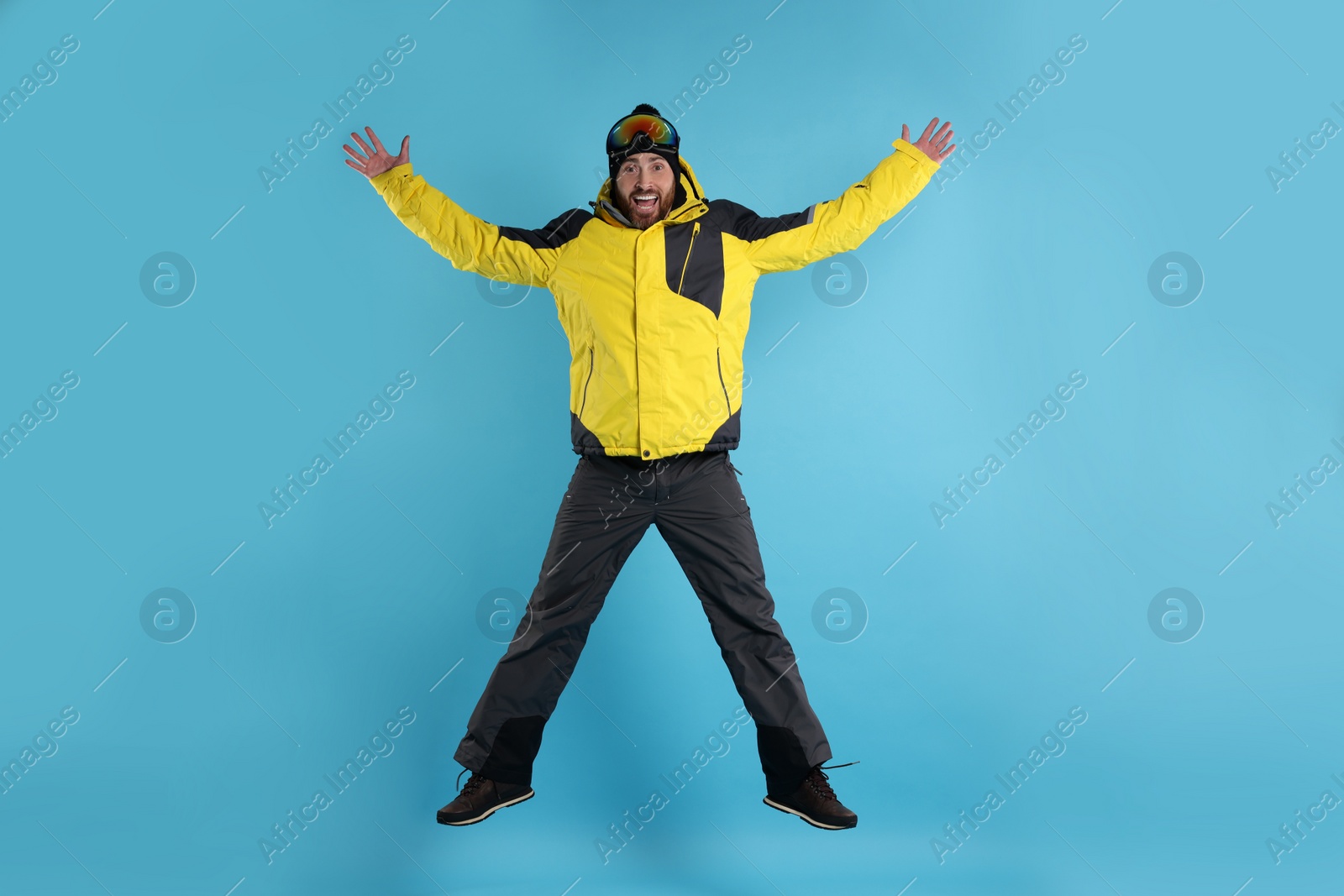 Photo of Winter sports. Man in ski suit and goggles jumping on light blue background