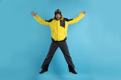 Photo of Winter sports. Man in ski suit and goggles jumping on light blue background