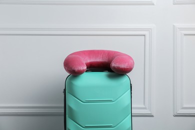 Photo of Pink travel pillow on turquoise suitcase near white wall