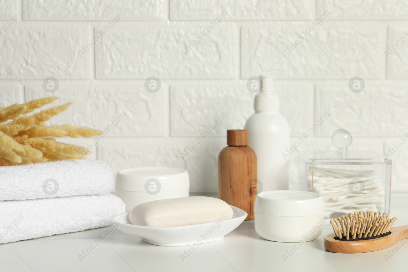 Photo of Different bath accessories, personal care products and spikelets on white table near brick wall