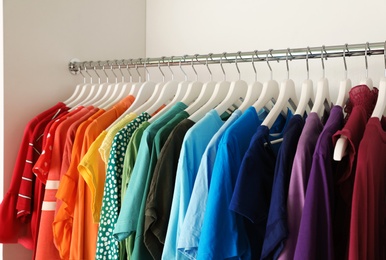 Photo of Hangers with different colorful clothes on rack in wardrobe