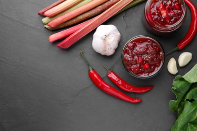 Photo of Tasty rhubarb sauce and ingredients on black table, flat lay. Space for text