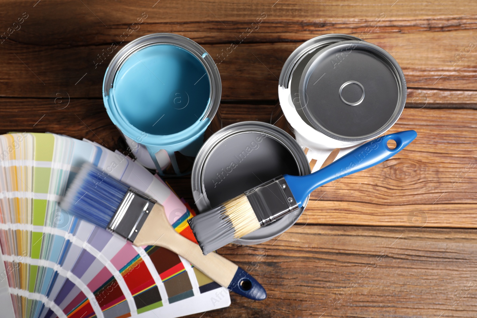 Photo of Cans of paints, brushes and color palette on wooden background, flat lay