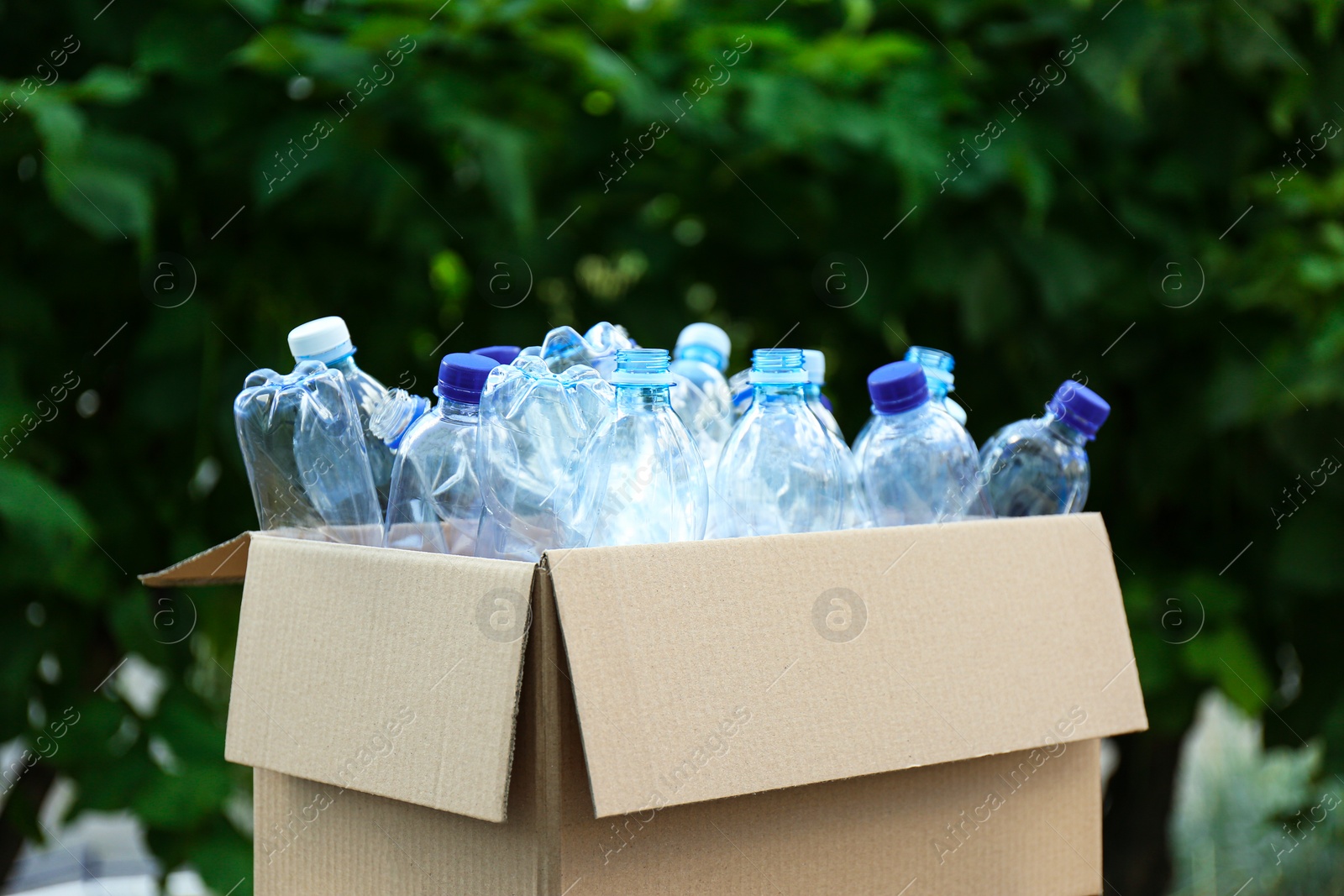 Photo of Cardboard box with used plastic bottles outdoors. Recycle concept