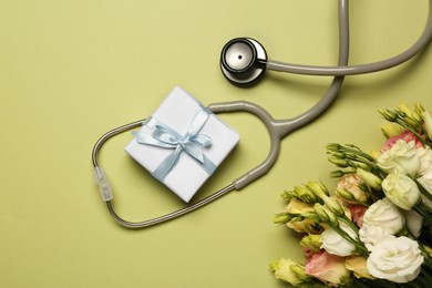 Photo of Stethoscope, gift box and eustoma flowers on light green background, flat lay. Happy Doctor's Day