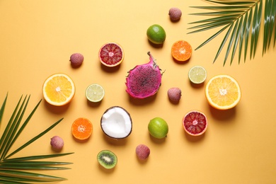 Photo of Different exotic fruits and palm leaves on beige background, flat lay