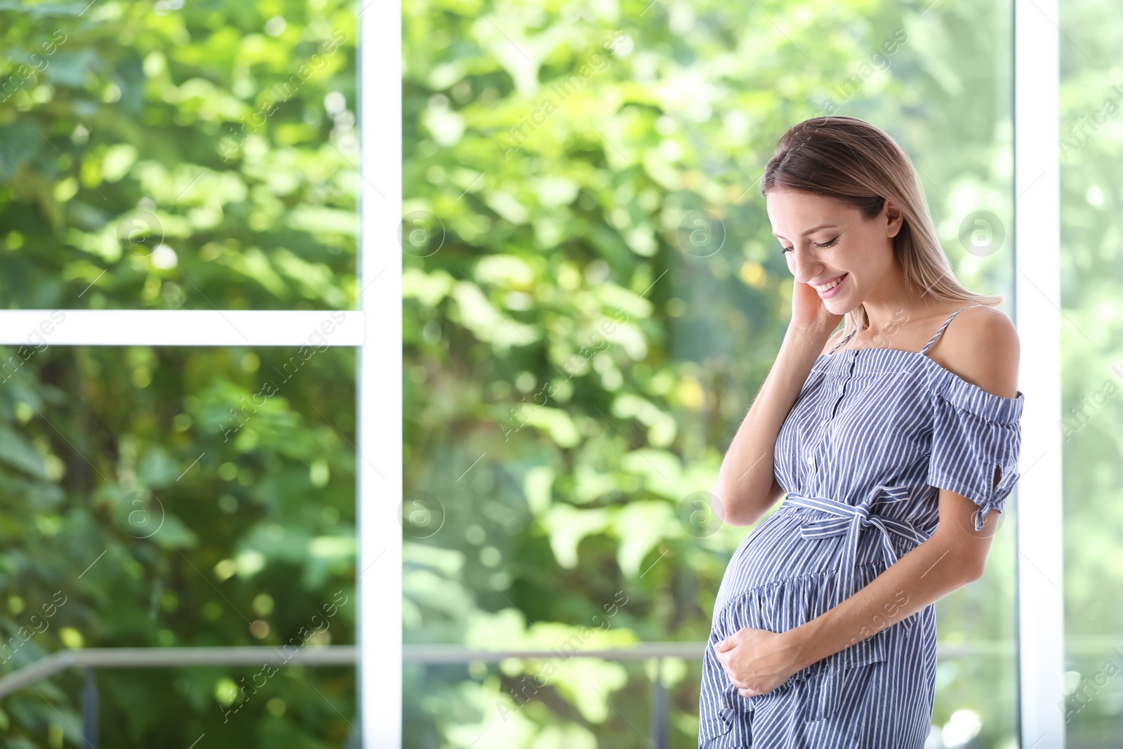 Photo of Happy pregnant woman standing near window at home