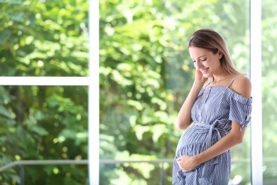 Happy pregnant woman standing near window at home