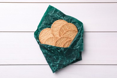 Photo of Tasty cookies in beeswax food wrap on white wooden table, top view