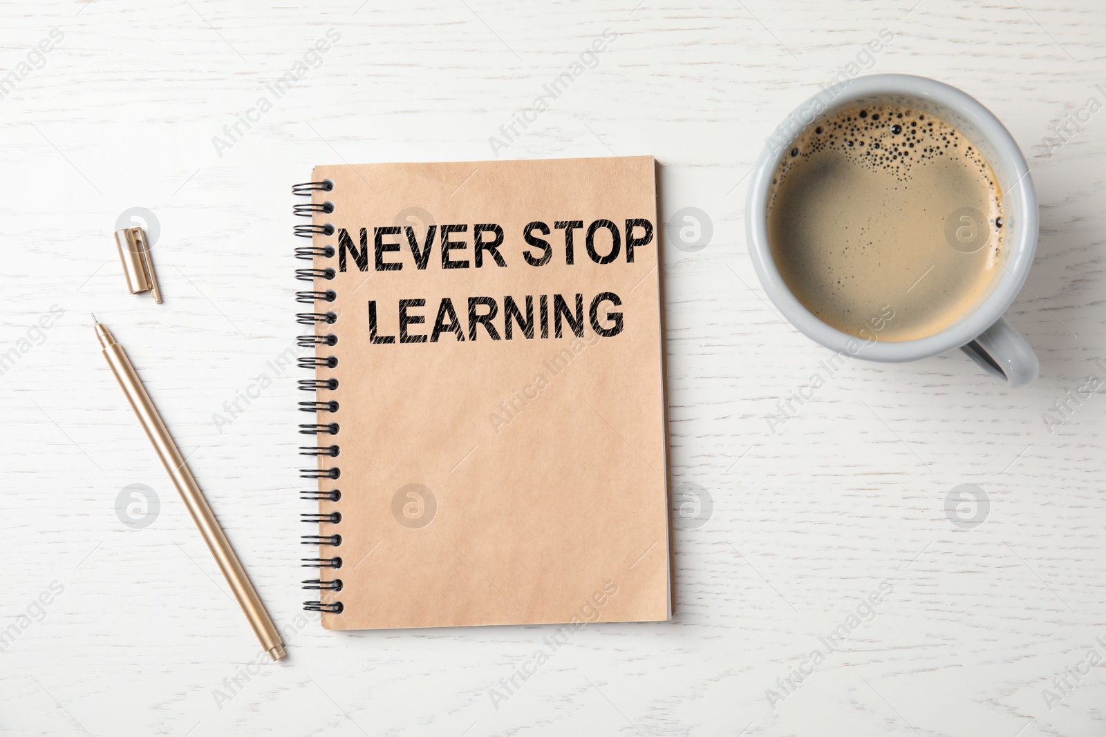Image of Notebook with phrase NEVER STOP LEARNING, pen and cup of coffee on white wooden background, flat lay
