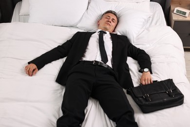 Businessman with briefcase sleeping on bed indoors