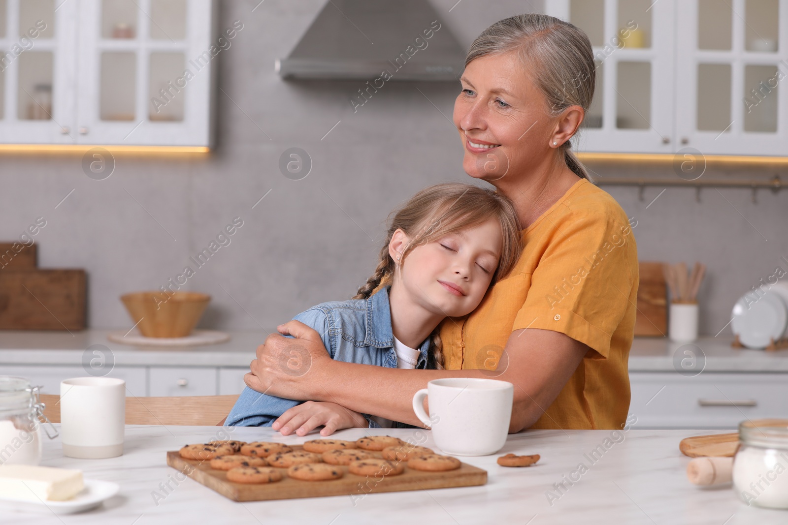 Photo of Happy grandmother hugging her granddaughter in kitchen