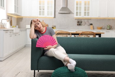 Photo of Woman waving pink hand fan to cool herself on sofa at home. Space for text