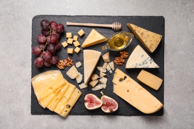 Slate board with different types of delicious cheese and snacks on grey table, top view