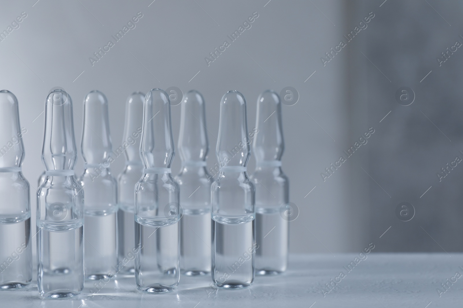 Photo of Pharmaceutical ampoules with medication on white table against grey background. Space for text