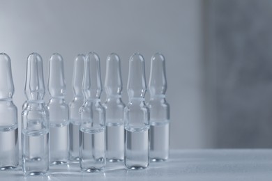 Photo of Pharmaceutical ampoules with medication on white table against grey background. Space for text