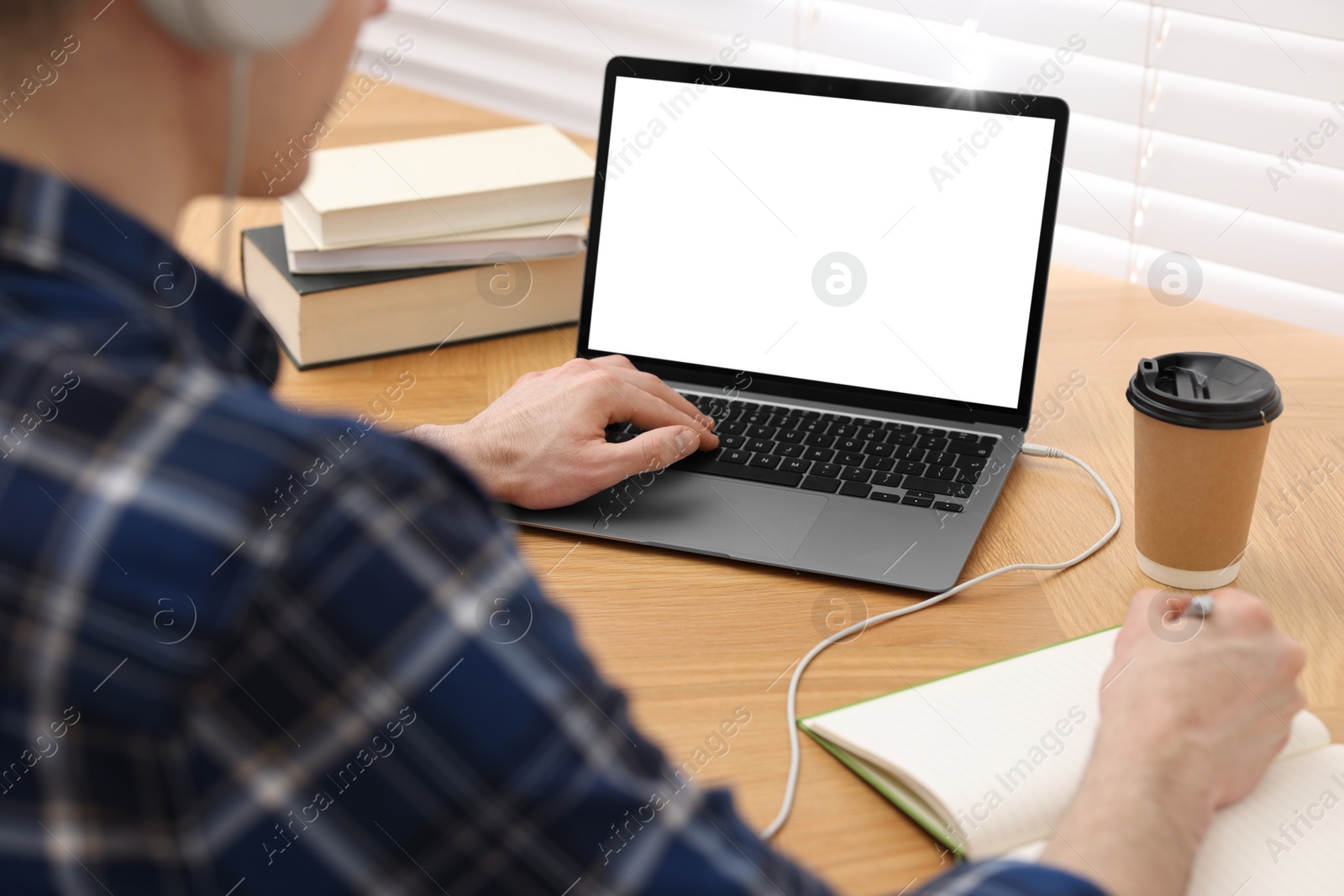 Photo of E-learning. Man taking notes during online lesson at table indoors, closeup