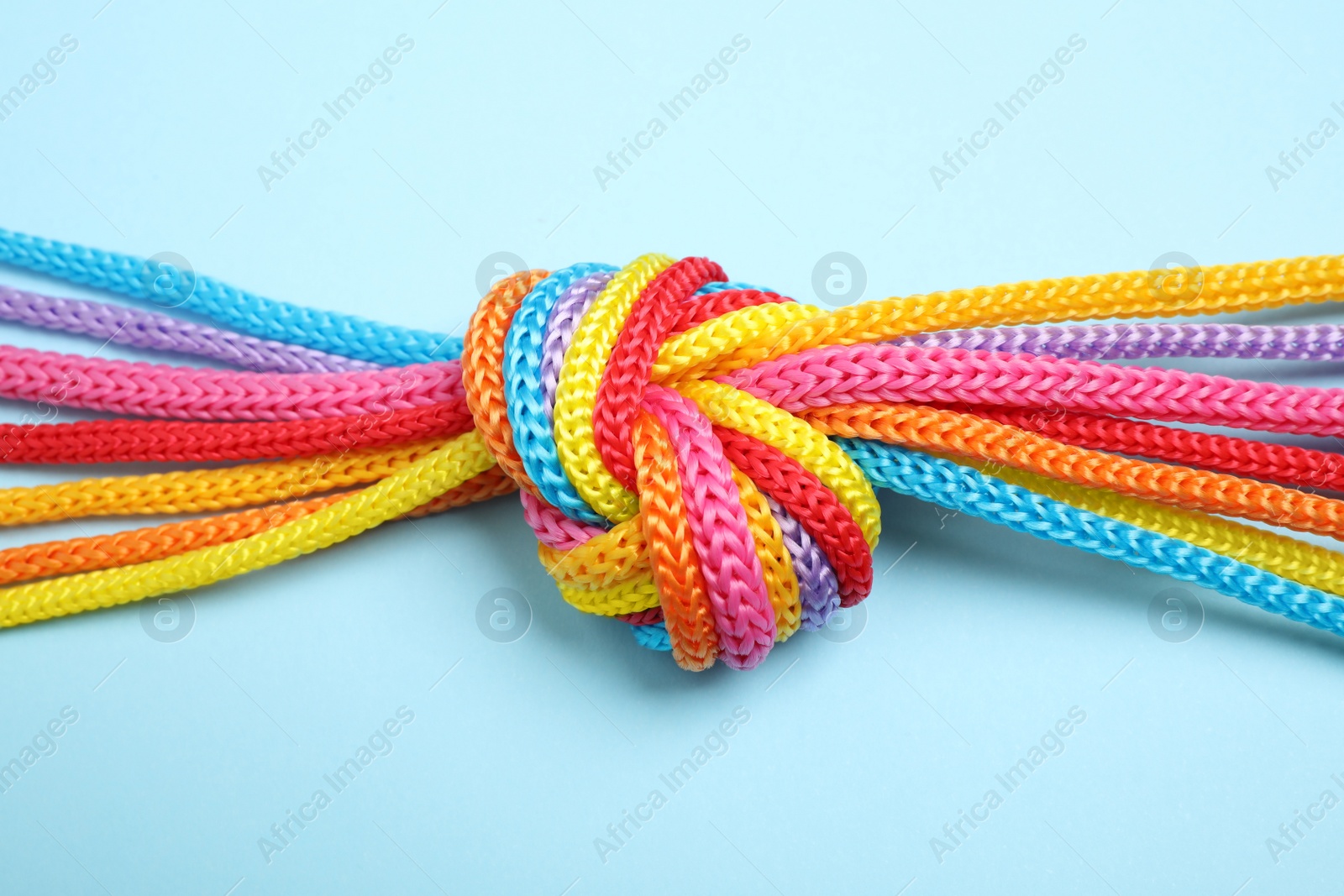 Photo of Colorful ropes tied together on light blue background, top view. Unity concept