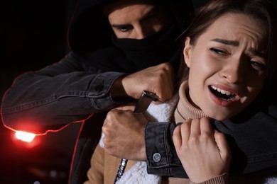 Photo of Criminal with knife attacking young woman outdoors at night. Self defense concept